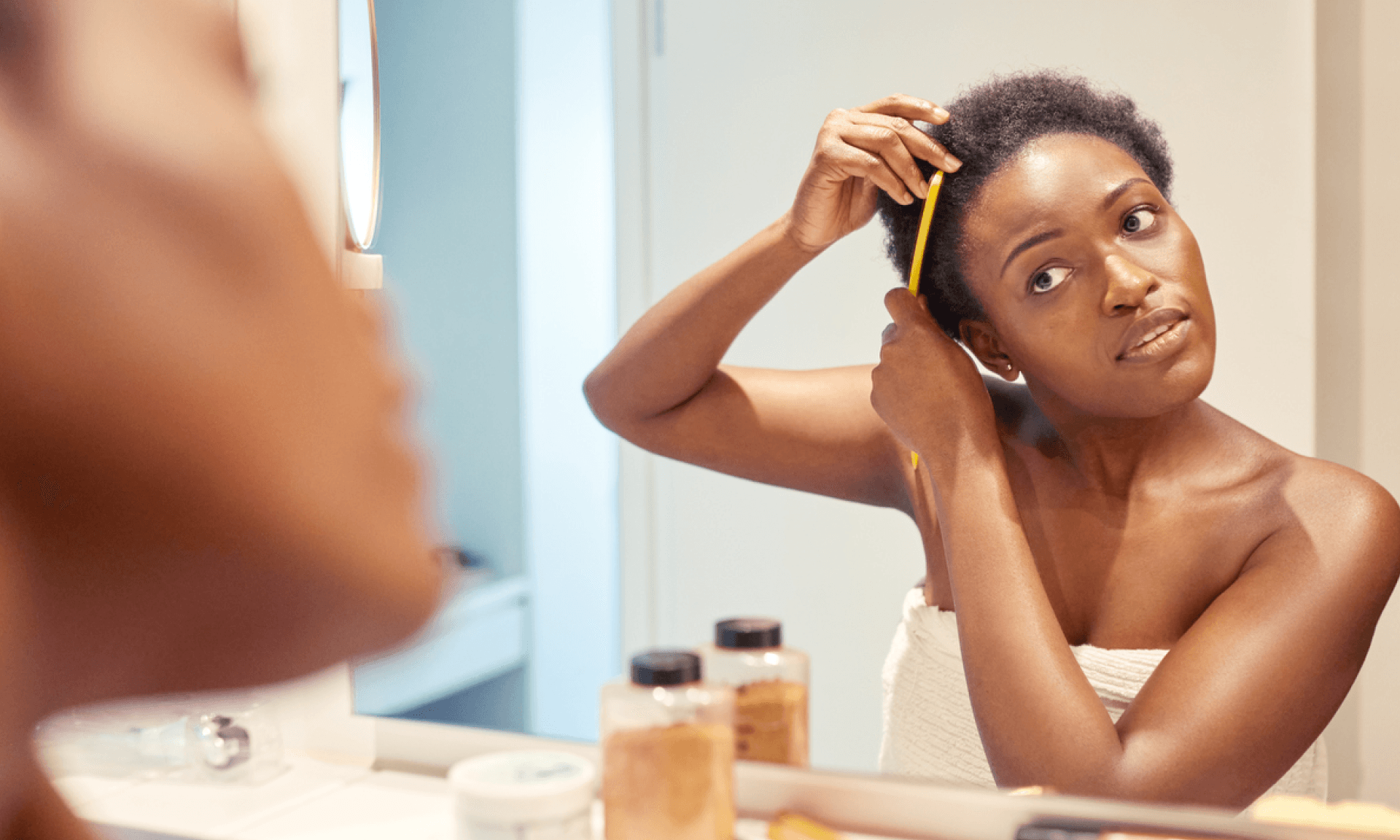 A Black woman combing her hair in the bathroom mirror