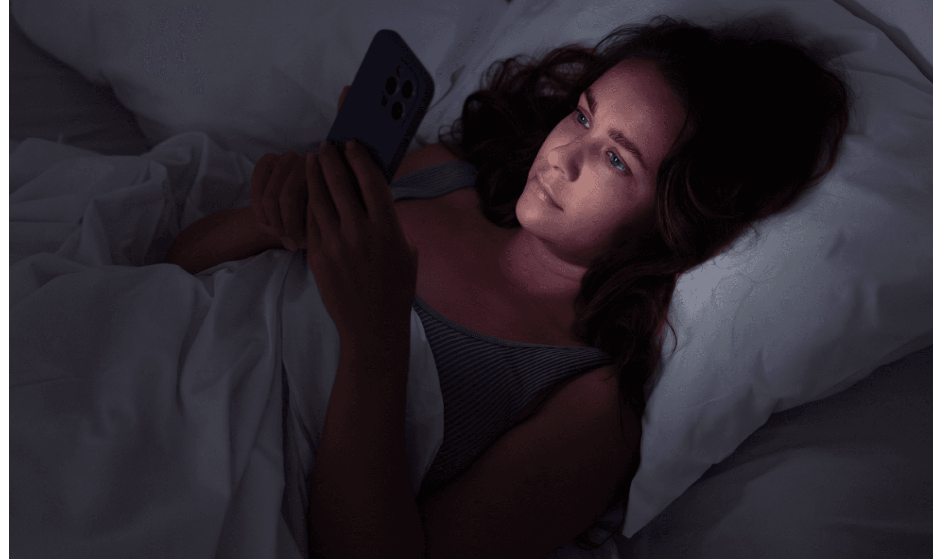 A woman laying in bed at night scrolling on her phone