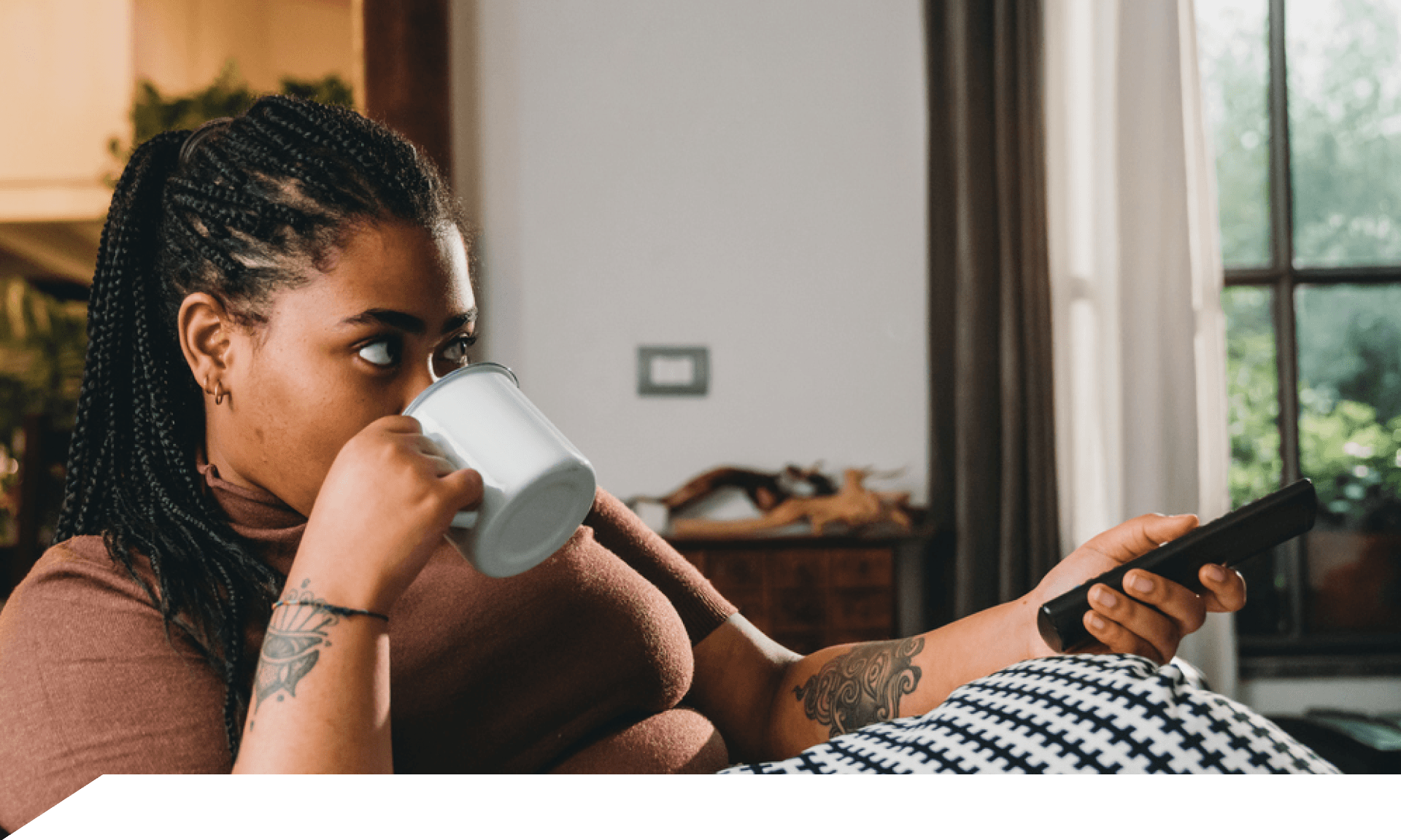 A woman sitting on the couch watching TV and drinking tea