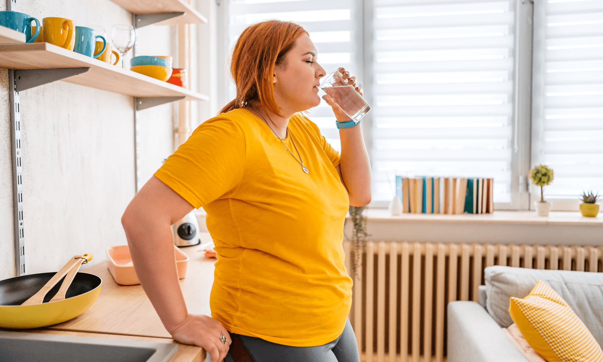 A woman leaning on her kitchen counter drinking a glass of water