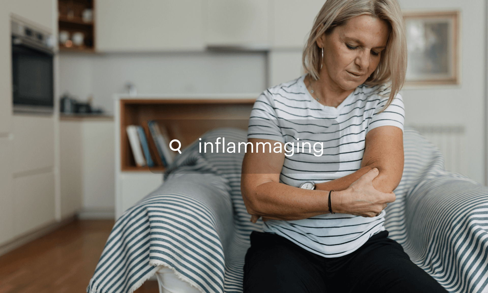 A woman sitting in an armchair holding her elbow in discomfort
